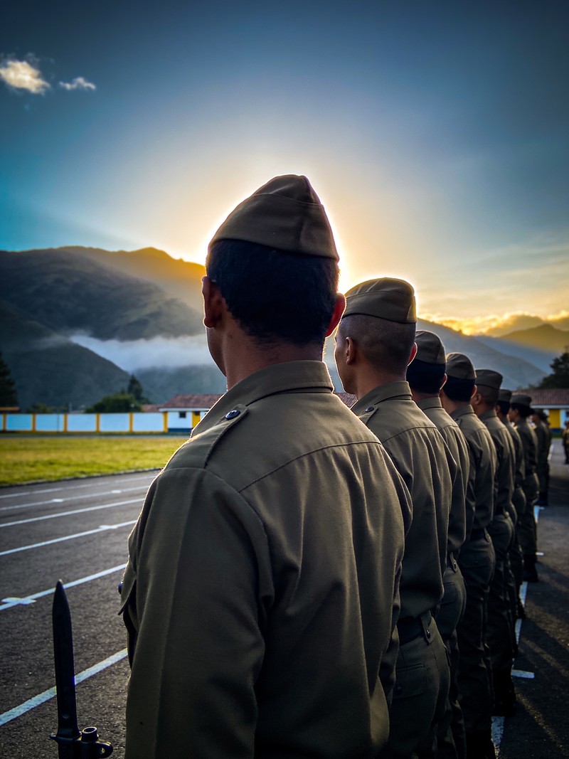 Uniformados en formación al amanecer vistos de espaldas en un paisaje andino, sin insignias visibles